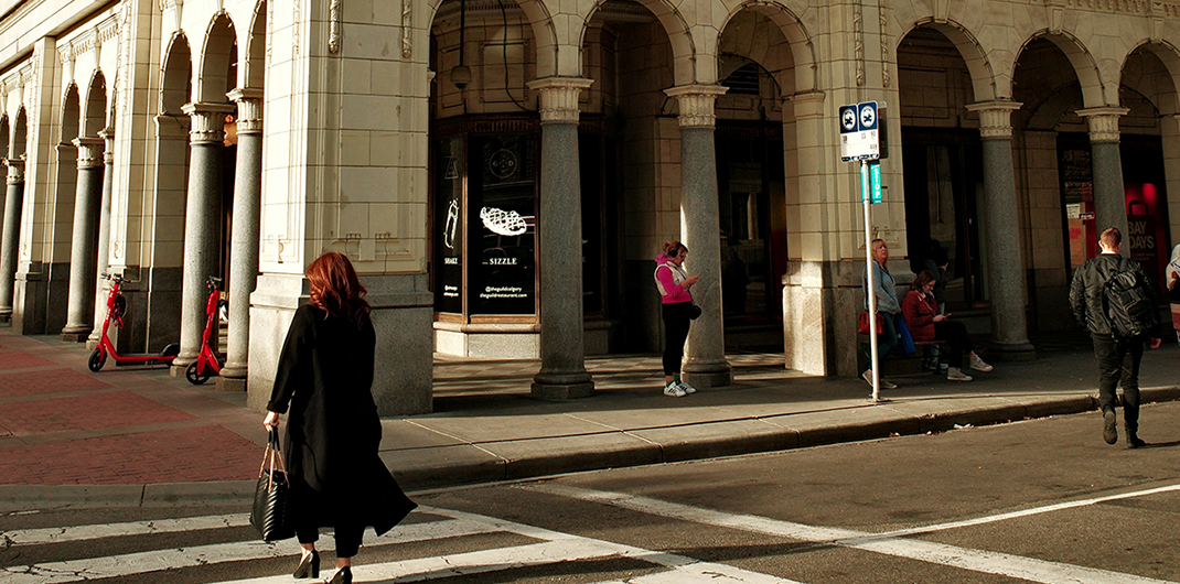 person crossing a crosswalk towards a storefront with classical architectural details